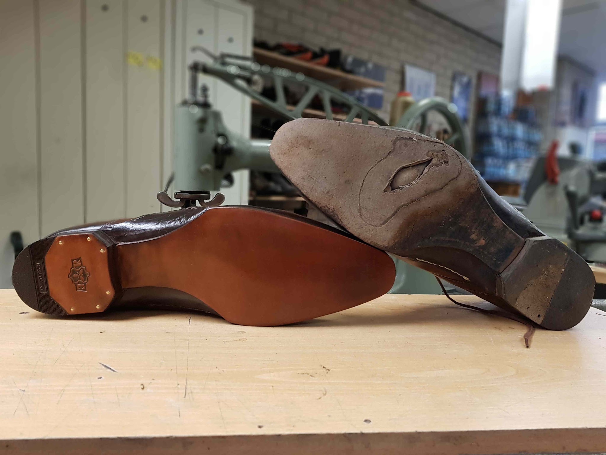 Een nette herenschoen met nieuwe leren zool en hak naast de versleten oude zool met een gat